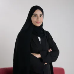 Athari Alqaydi posing for a photo with greyish studio background and a portion of a red sofa.