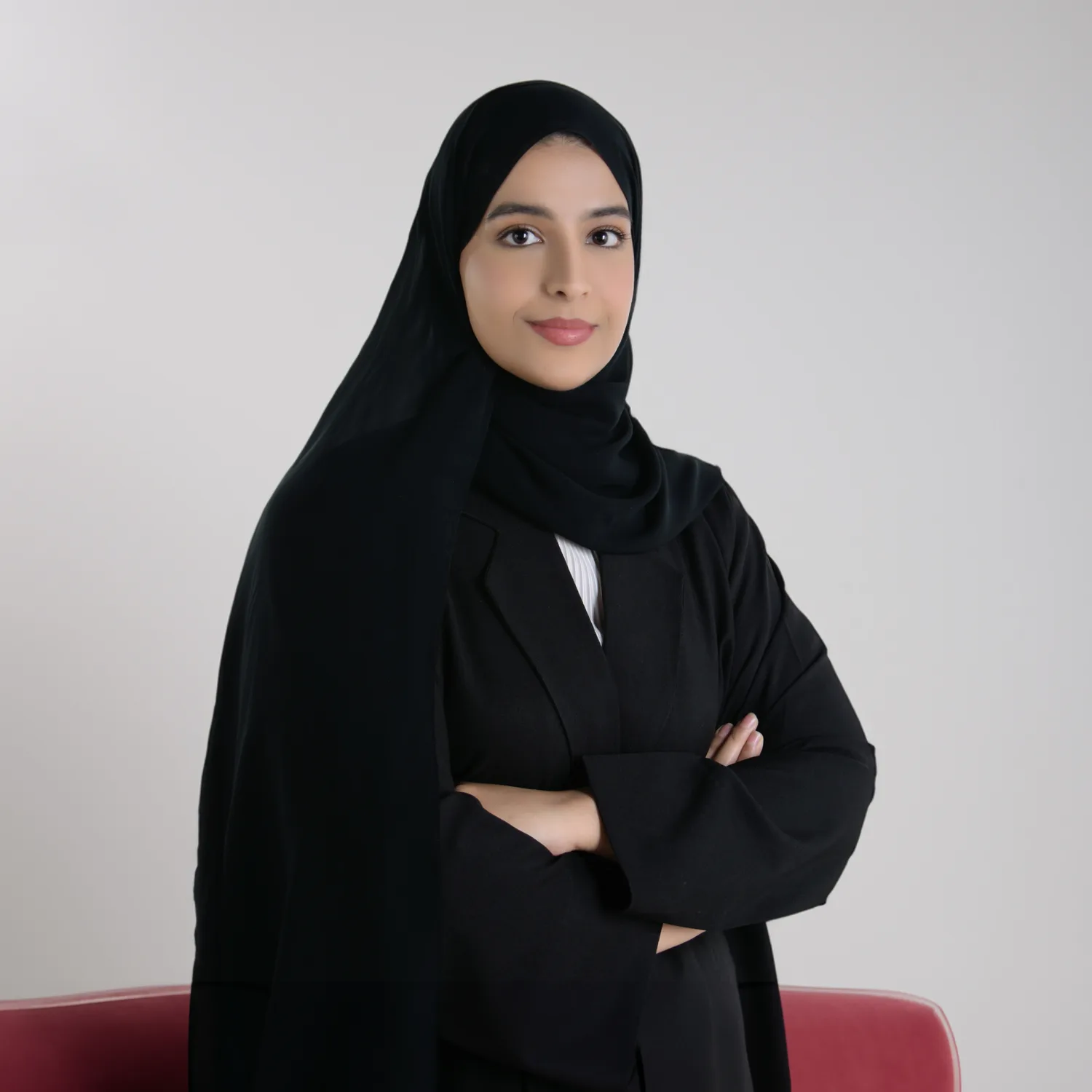Athari Alqaydi posing for a photo with greyish studio background and a portion of a red sofa.