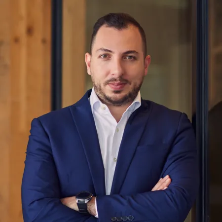 Mario Saab wearing a blue suit while standing in-front of a glass wall