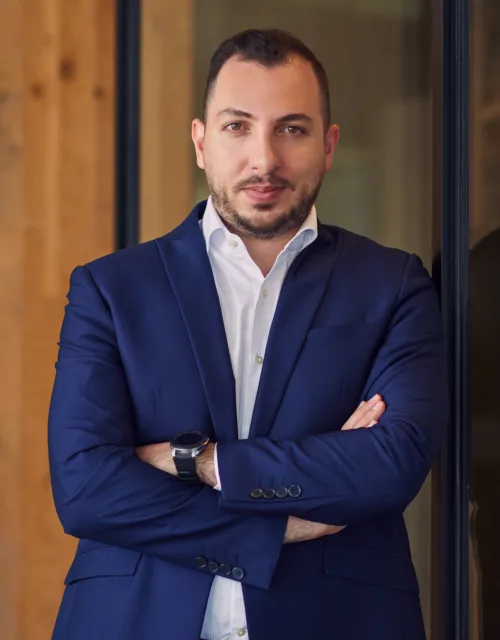 Mario Saab wearing a blue suit while standing in-front of a glass wall