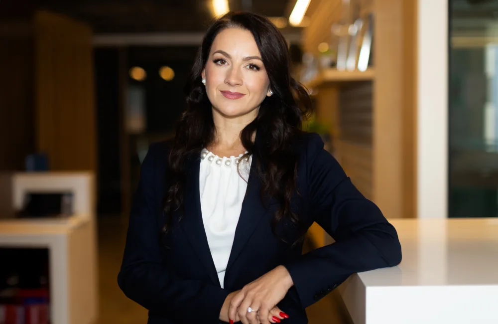 Olga in a white top and dark jacket looking to camera in the office