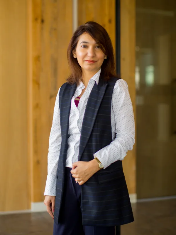 Rabia posing in front of a wooden wall in a white shirt and waistcoat