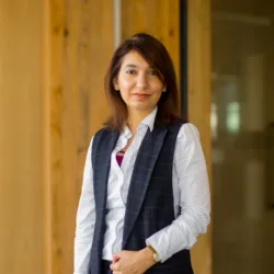 Rabia posing in front of a wooden wall in a white shirt and waistcoat