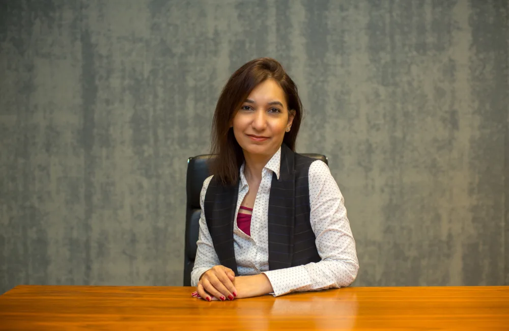 Rabia sat at a wooden table in a white shirt and waistcoat