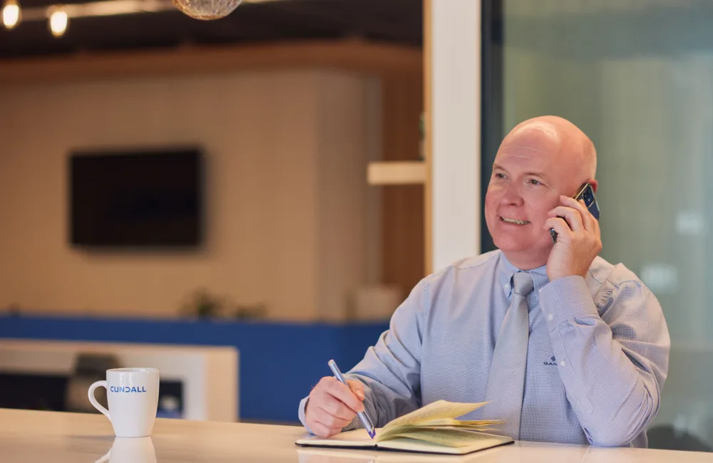 Richard Stratton smiling while talking on a mobile phone and taking notes