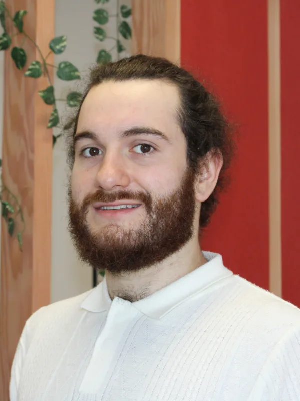 Adam Mullery smiling to camera in a white top with wooden beams and red and white walls in the background