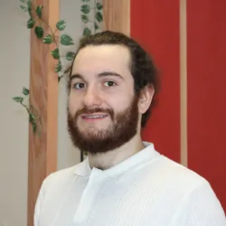 Adam Mullery smiling to camera in a white top with wooden beams and red and white walls in the background