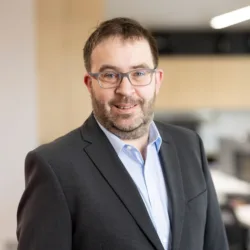 David in an open collar shirt and suit jacket stood in the Dublin office