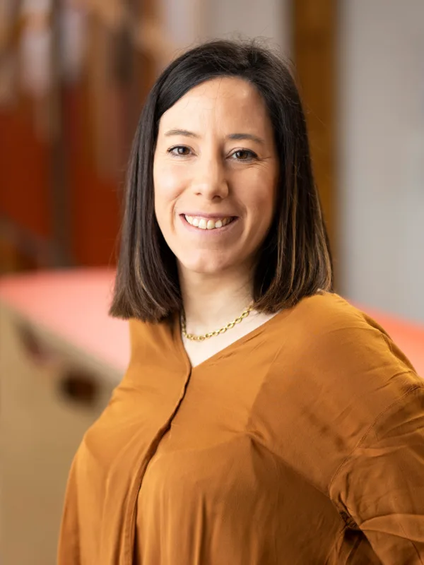 Ester smiling to camera in a long sleeve mustard top with the office behind