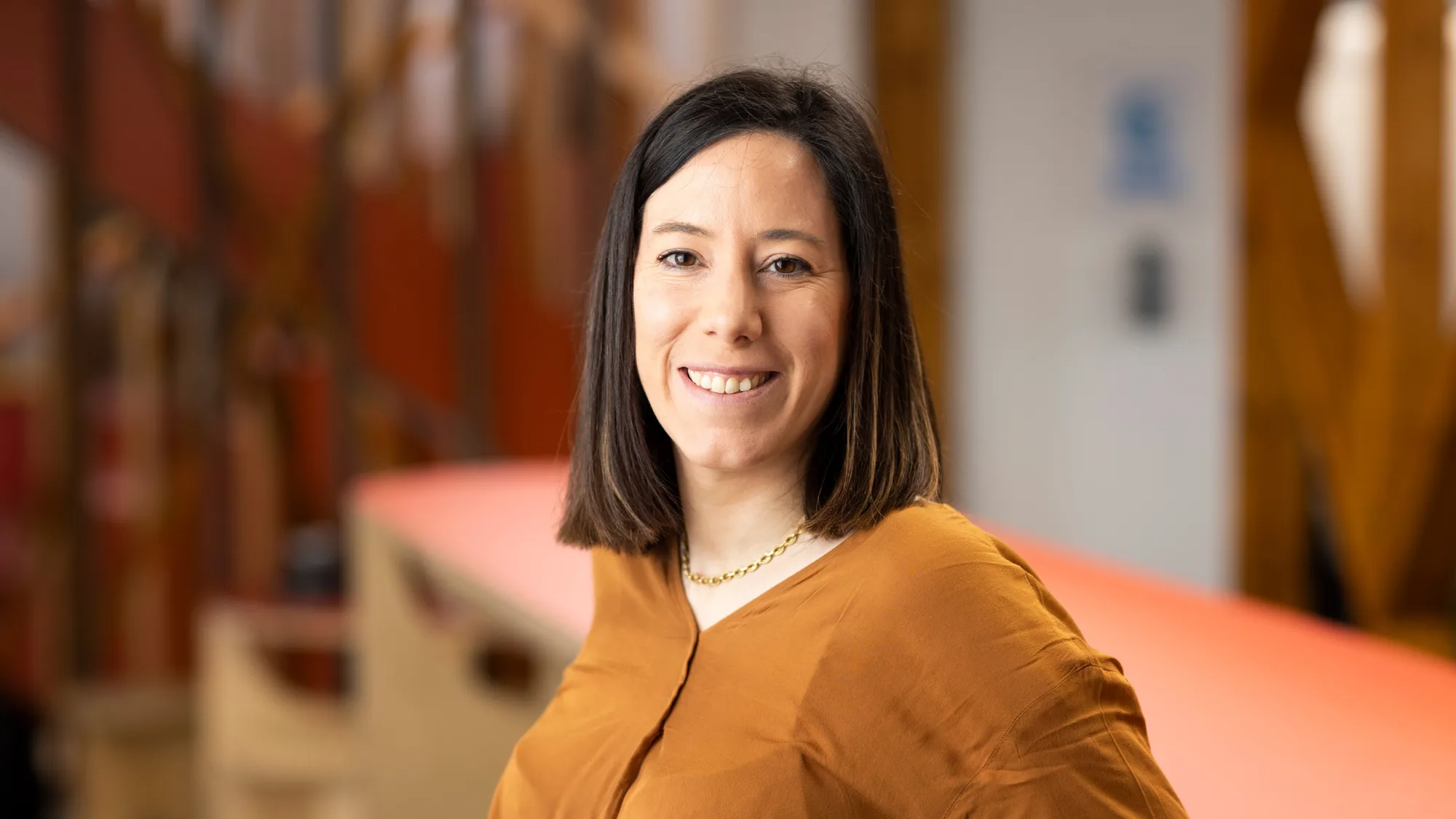Ester smiling to camera in a long sleeve mustard top with the office behind