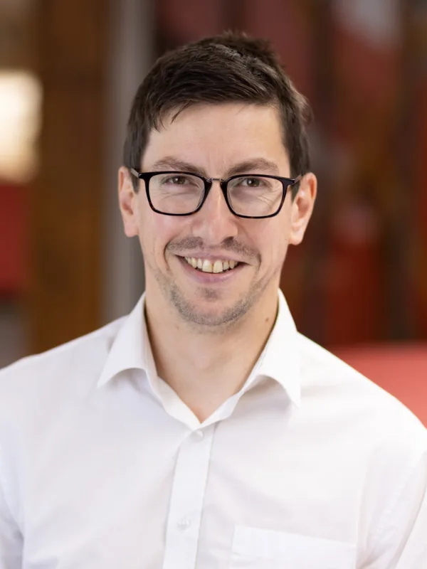 Gerard Doyle in shirt with a blurred office kitchen background which is red