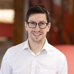 Gerard Doyle in shirt with a blurred office kitchen background which is red