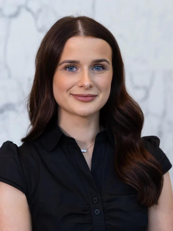 Professional head-and-shoulders portrait of a person with dark hair wearing a black shirt against a light marble background.