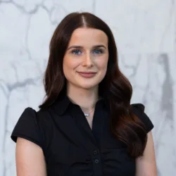 Professional head-and-shoulders portrait of a person with dark hair wearing a black shirt against a light marble background.