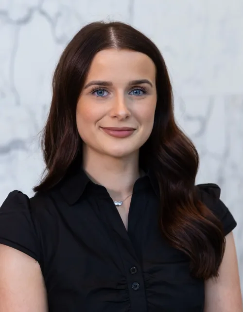 Professional head-and-shoulders portrait of a person with dark hair wearing a black shirt against a light marble background.