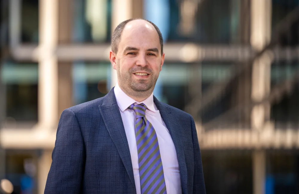 Duncan wearing a purple shirt and tie and suit jacket