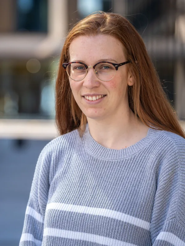 Holly in front of the office exterior wearing a grey jumper with white horizontal stripes.