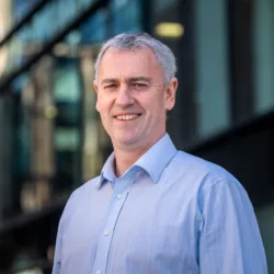 John McLoughlin looking towards the camera in a blue shirt