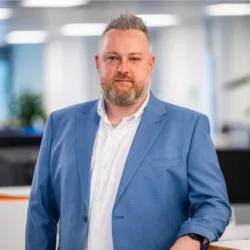 Keith Richardson standing in the Edinburgh office in a white shirt and blue blazer