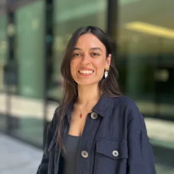 Lucia smiling in front of the glazed office in a large button open collared navy shirt.