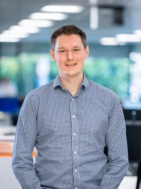 Patrick smiling for a photo with computer monitors and office desks in the background.