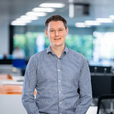 Patrick smiling for a photo with computer monitors and office desks in the background.
