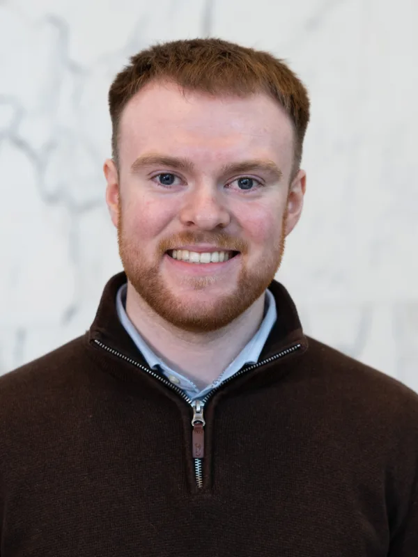 Head-and-shoulders portrait of a person wearing a dark quarter-zip sweater against a light marble-patterned background.