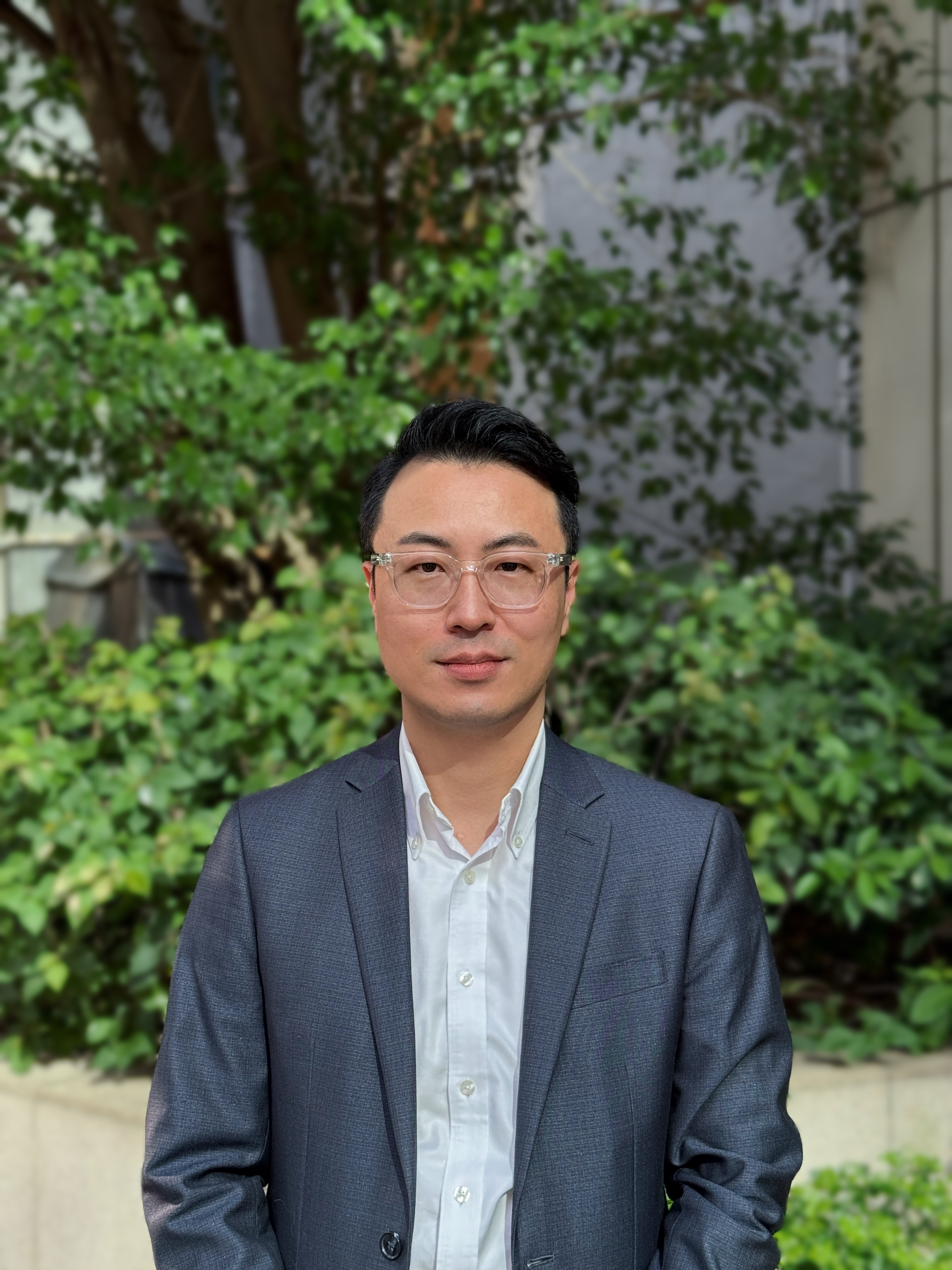 Byeonghee in a shirt and suit jacket looking to camera outside