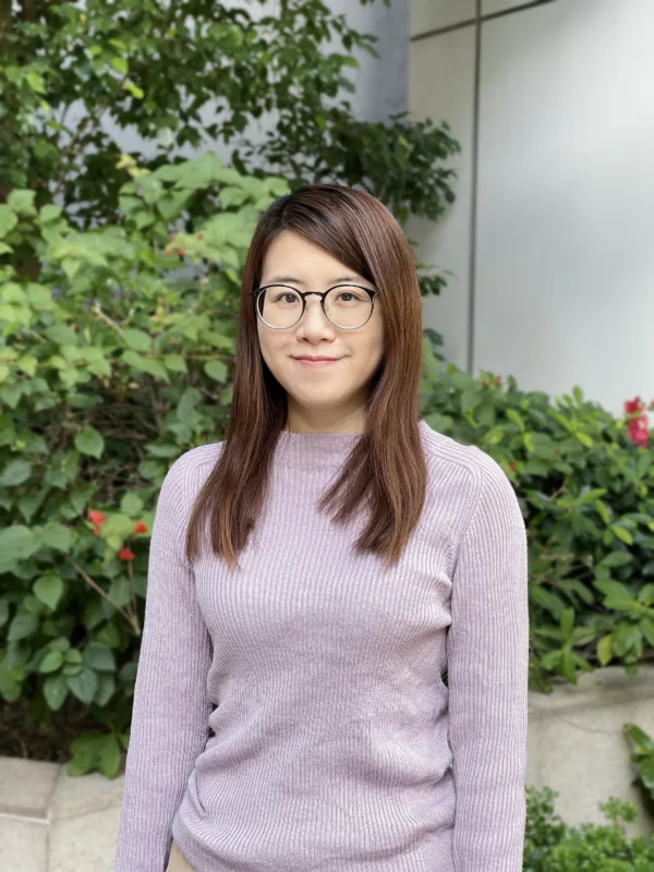 Headshot of Hannah in a purple jumper, in front of some plants.