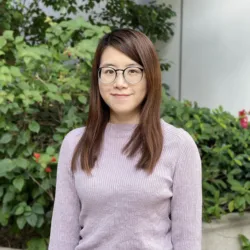Headshot of Hannah in a purple jumper, in front of some plants.