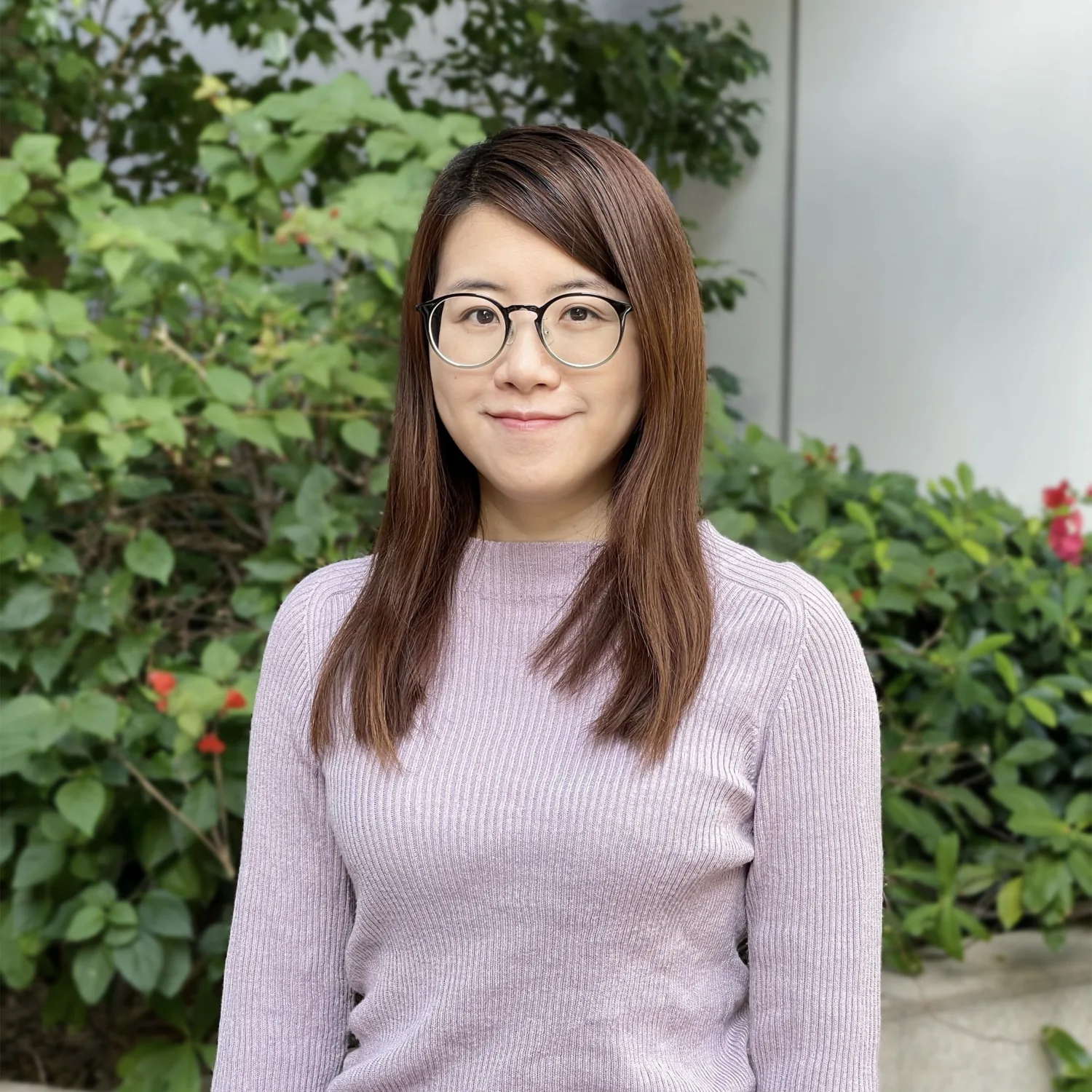 Headshot of Hannah in a purple jumper, in front of some plants.