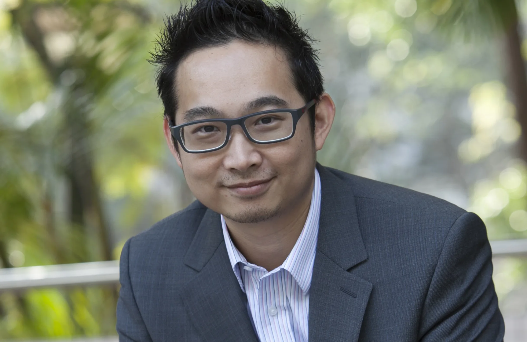 Joe Tang in a grey suit and pale shirt with blurred green park background
