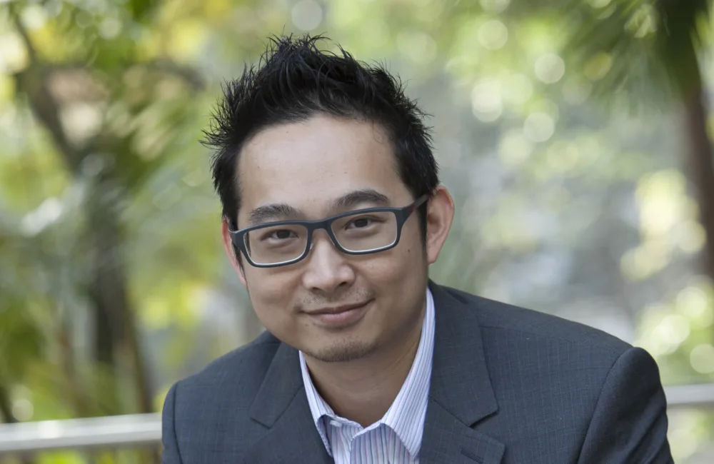 Joe Tang in a grey suit and pale shirt with blurred green park background