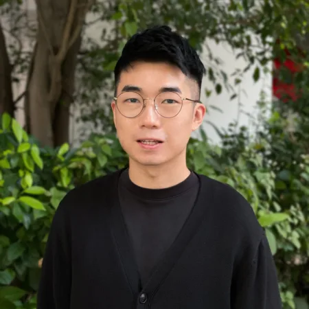 Pete wearing a dark round neck tee and cardigan outside in front of greenery
