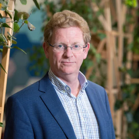Alan Fogarty in London office reception in a suit witch wooden terrace panelling for plants in background