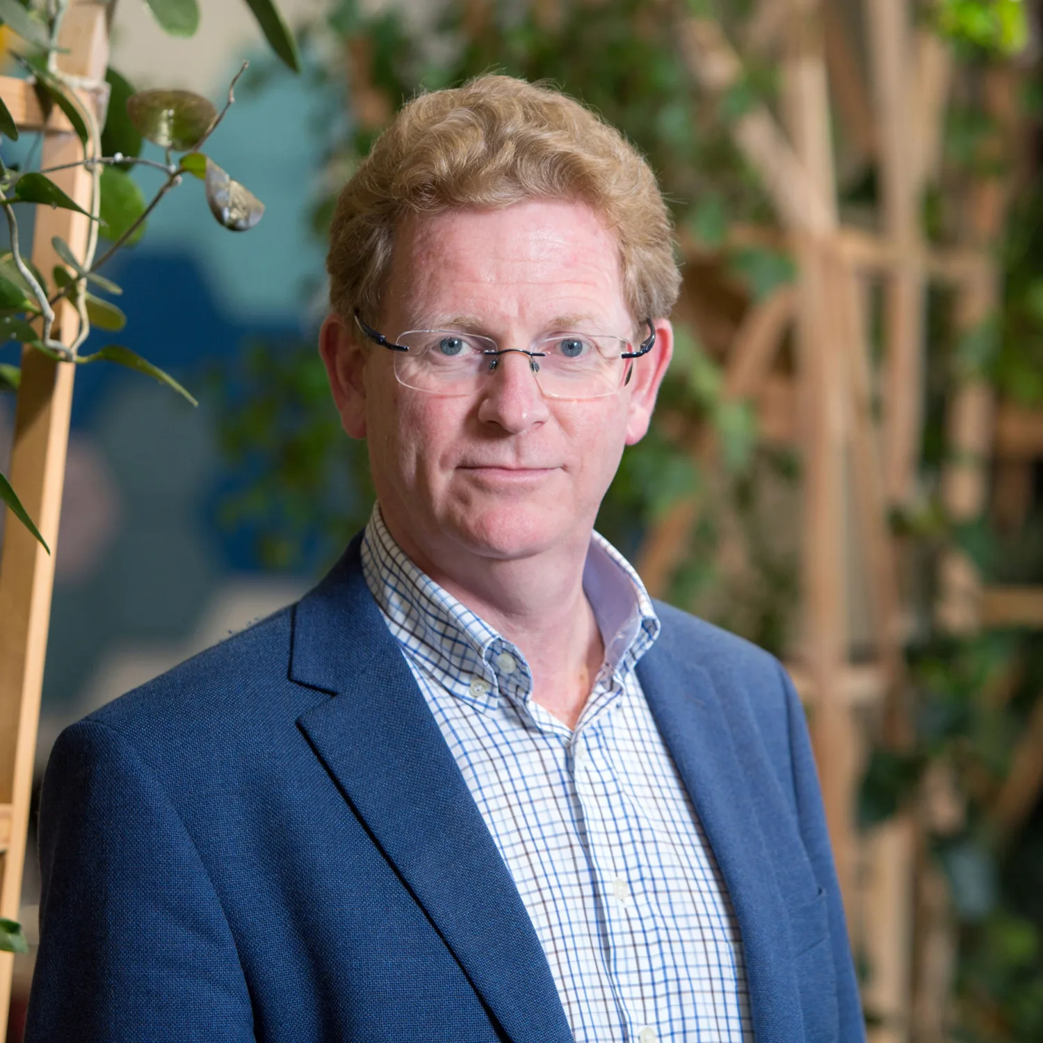 Alan Fogarty in London office reception in a suit witch wooden terrace panelling for plants in background
