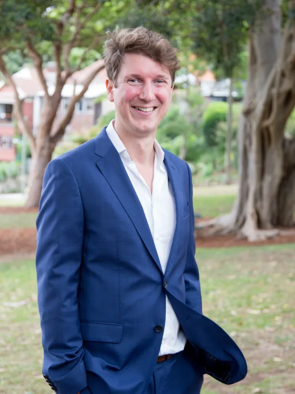 Alan wearing a white open collar shirt and blue suit in a suburban park