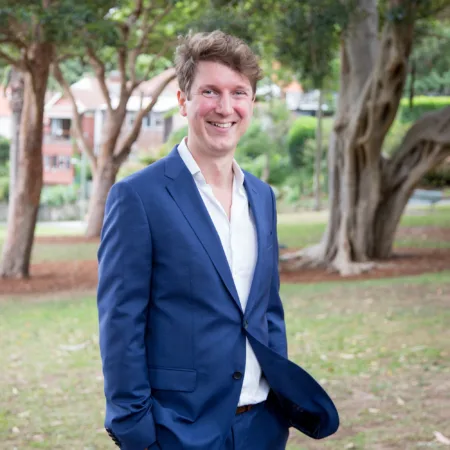 Alan wearing a white open collar shirt and blue suit in a suburban park