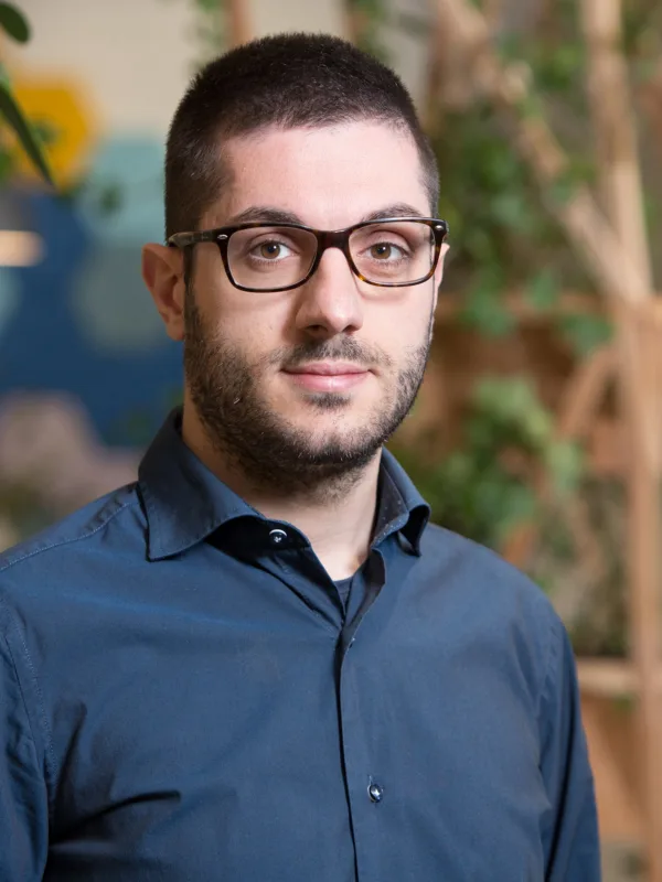 Danilo Cava in London office reception wearing a dark blue shirt with wooden panelling and plants in background