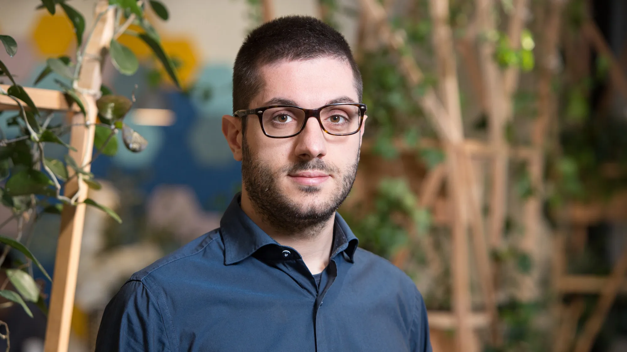 Danilo Cava in London office reception wearing a dark blue shirt with wooden panelling and plants in background