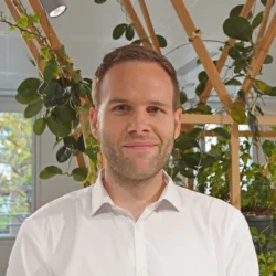 David in a white open collar shirt in front of an interior plant trellis