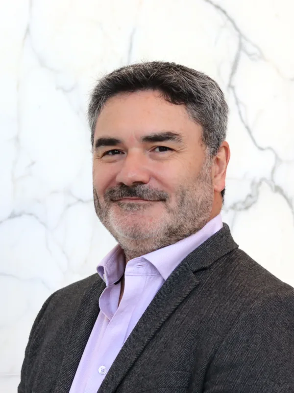 Head and shoulders shot of Drew against a white marble background wearing a pale pink shirt and grey blazer