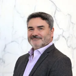 Head and shoulders shot of Drew against a white marble background wearing a pale pink shirt and grey blazer