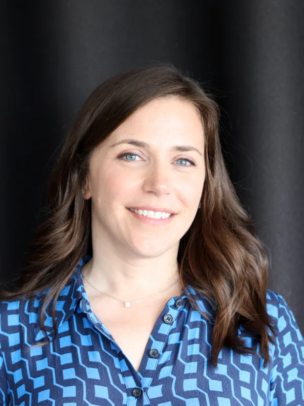 Frances in a blue buttoned top in front of a dark fabric wall