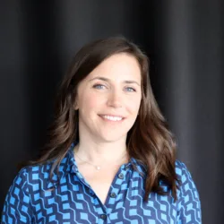 Frances in a blue buttoned top in front of a dark fabric wall