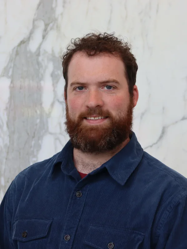 James in a dark blue open collar shirt in front of a marble wall