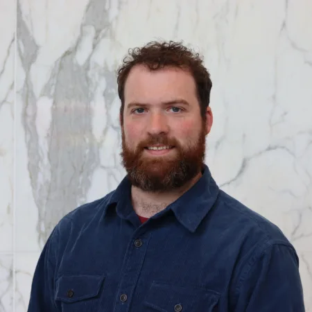 James in a dark blue open collar shirt in front of a marble wall