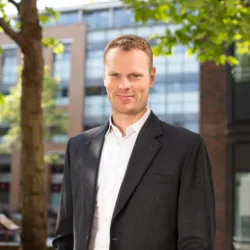 Jonnie Allen underneath a tree with buildings in the background.