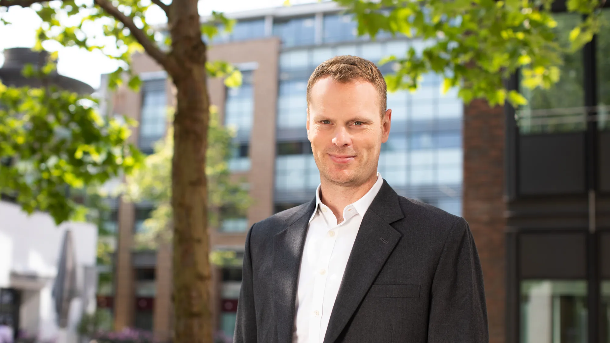 Jonnie Allen underneath a tree with buildings in the background.