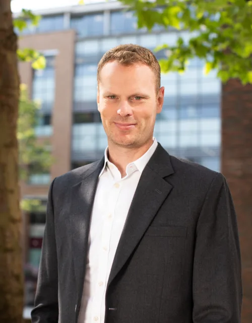 Jonnie Allen underneath a tree with buildings in the background.